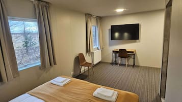 Ein Hotelzimmer mit Bett, Schreibtisch, Stuhl, Fernseher und einem Fenster mit Vorhängen.