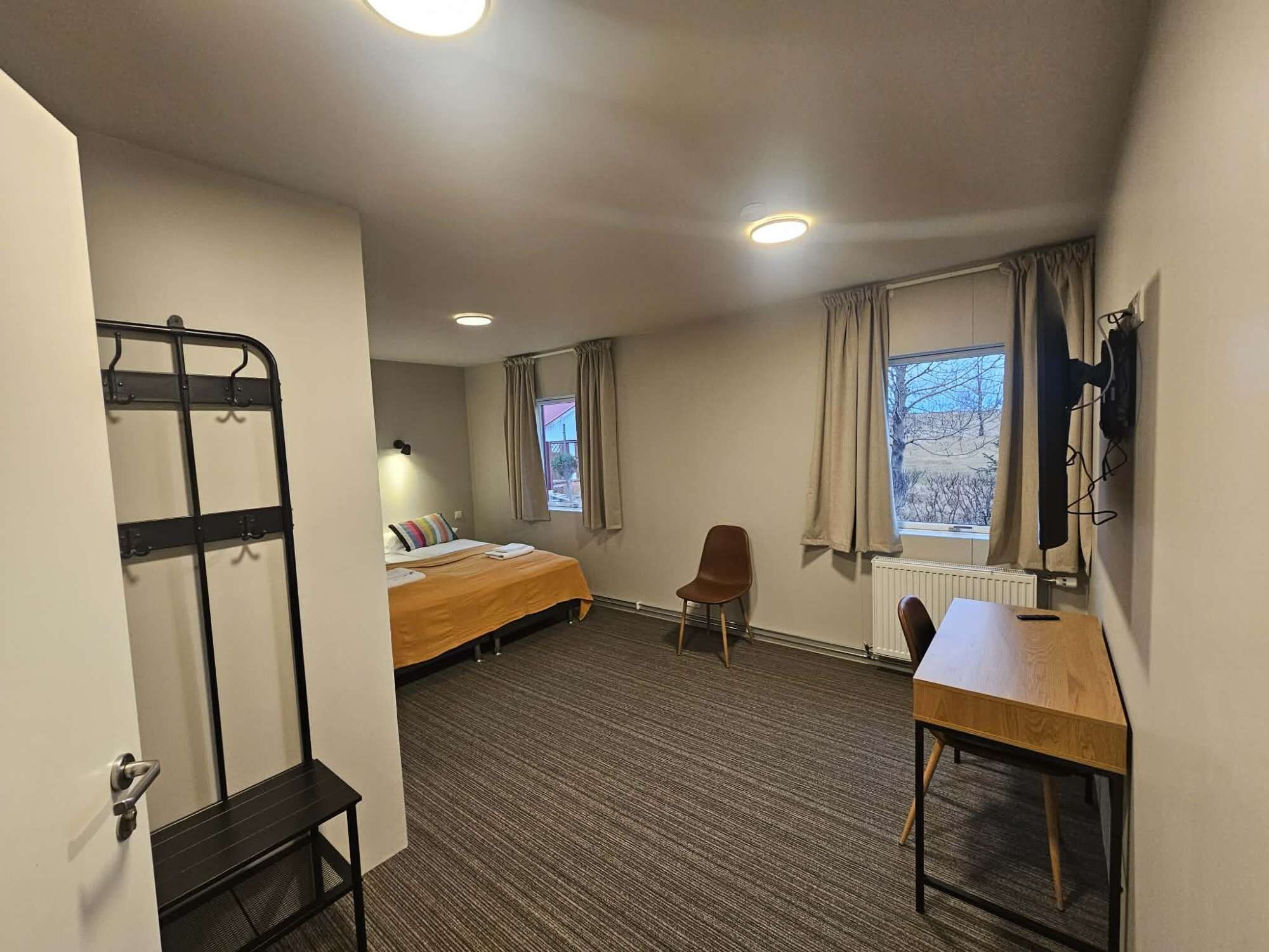 Ein Hotelzimmer mit Etagenbett, Schreibtisch, Stuhl, Heizkörper und einem Vorhangfenster.