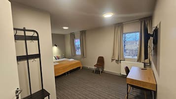 Ein Hotelzimmer mit Etagenbett, Schreibtisch, Stuhl, Heizkörper und einem Vorhangfenster.