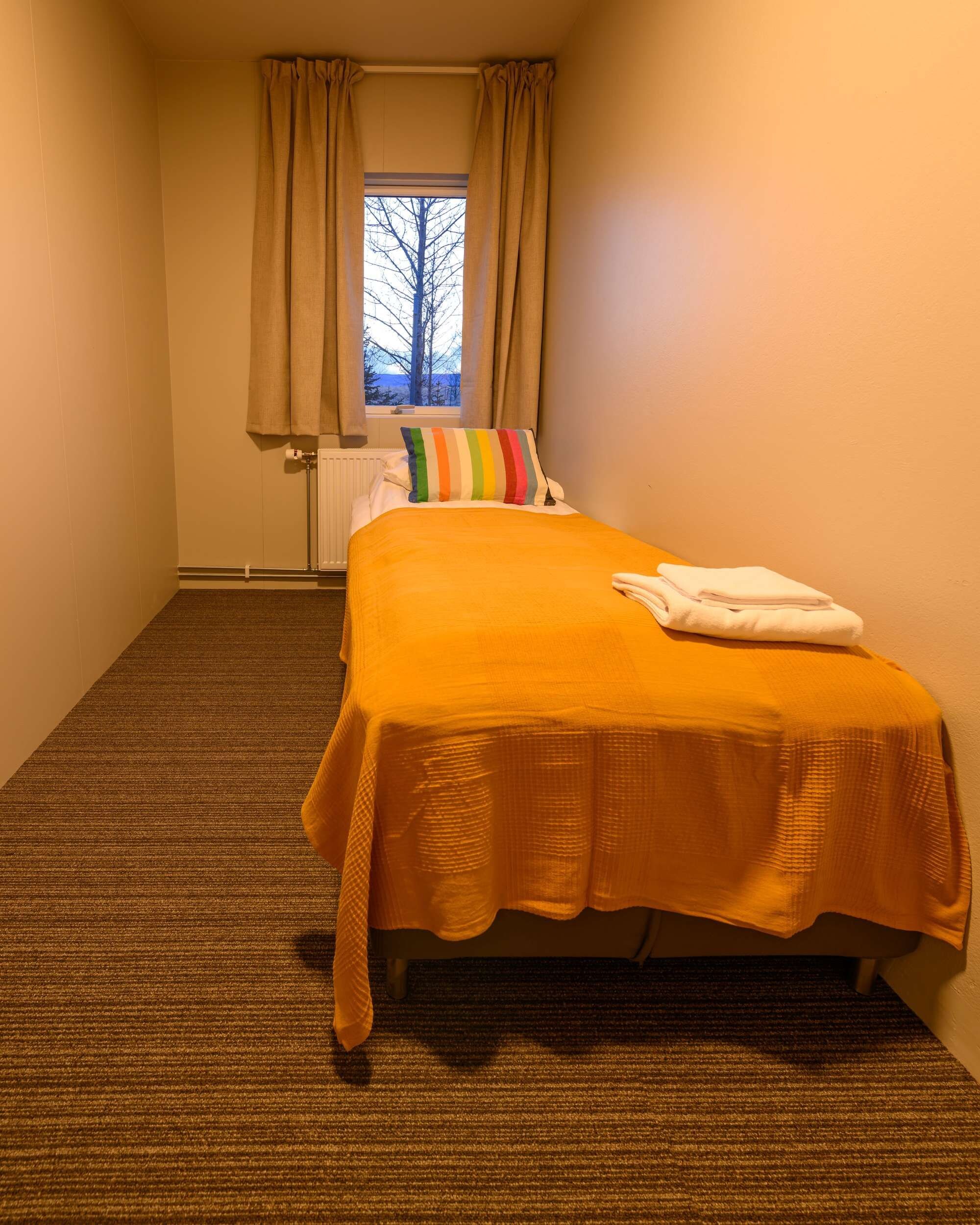 Ein Hotelzimmer mit einem Einzelbett, einem Fenster mit Vorhängen, einem Heizkörper und Teppichboden.