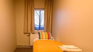 Ein Hotelzimmer mit einem Einzelbett, einem Fenster mit Vorhängen, einem Heizkörper und Teppichboden.