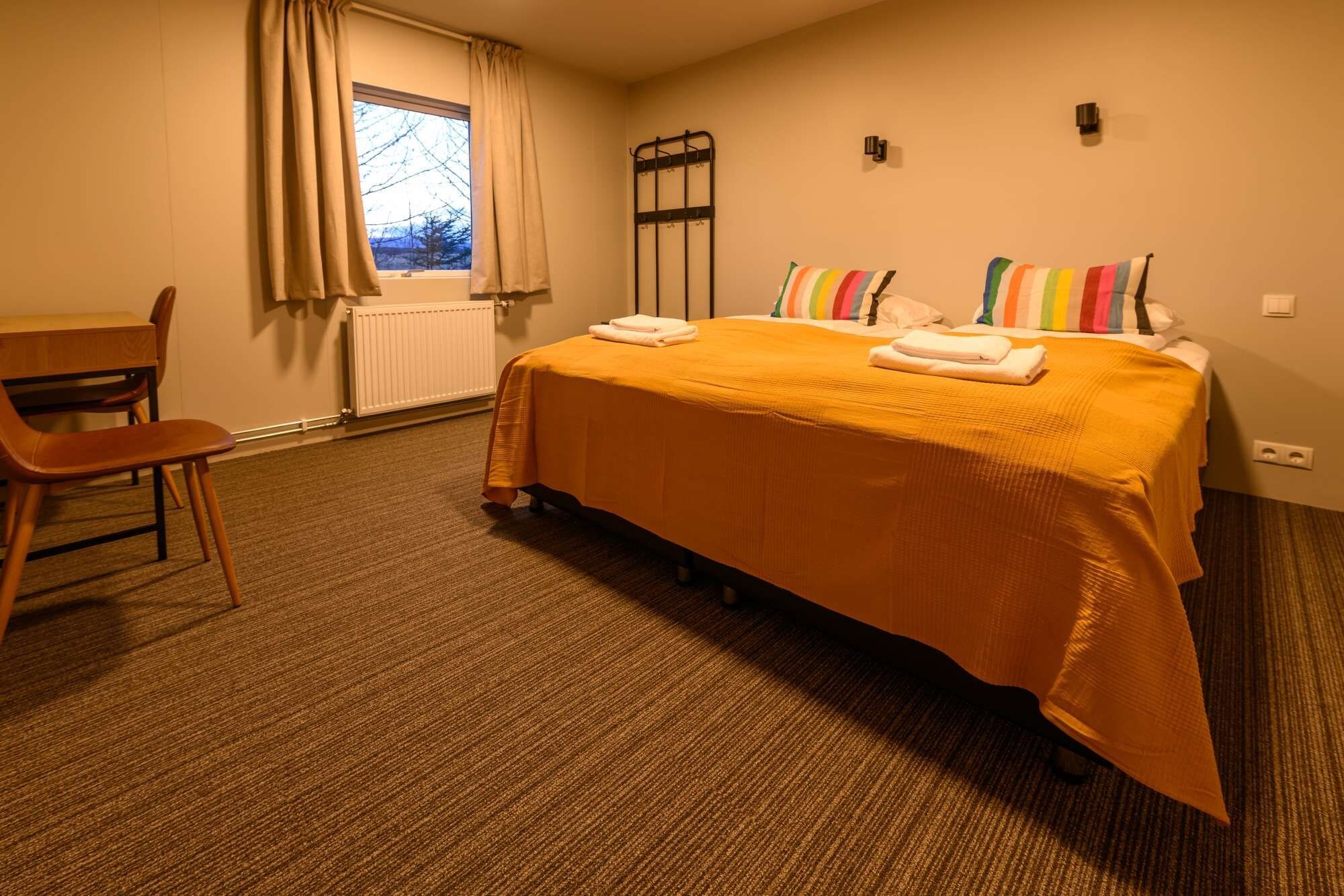 A hotel room with a bed, a chair, a radiator, and a window with curtains.