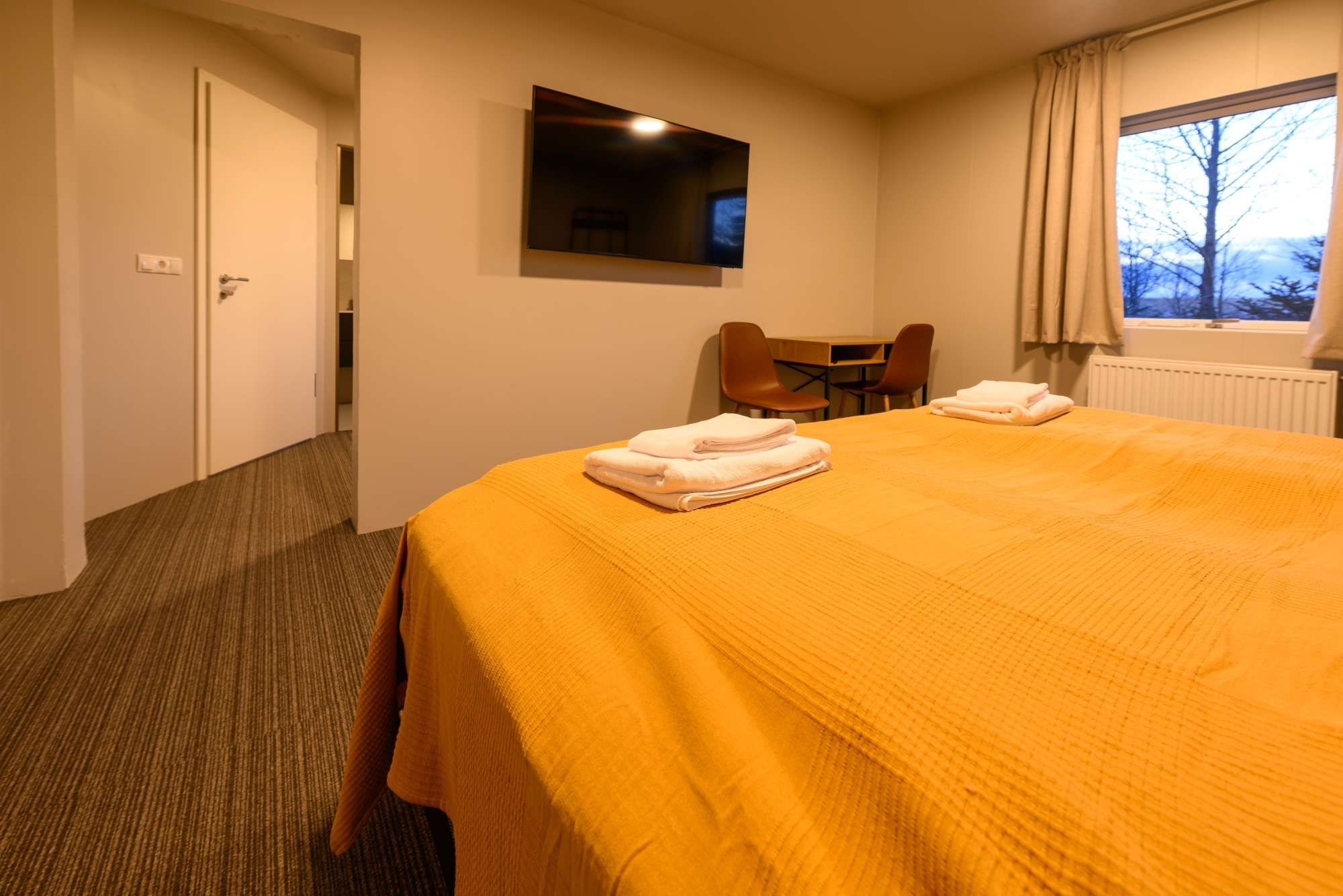 Ein Hotelzimmer mit einem Bett, einem an der Wand montierten Fernseher, einem Fenster mit Vorhängen und einem Sessel.