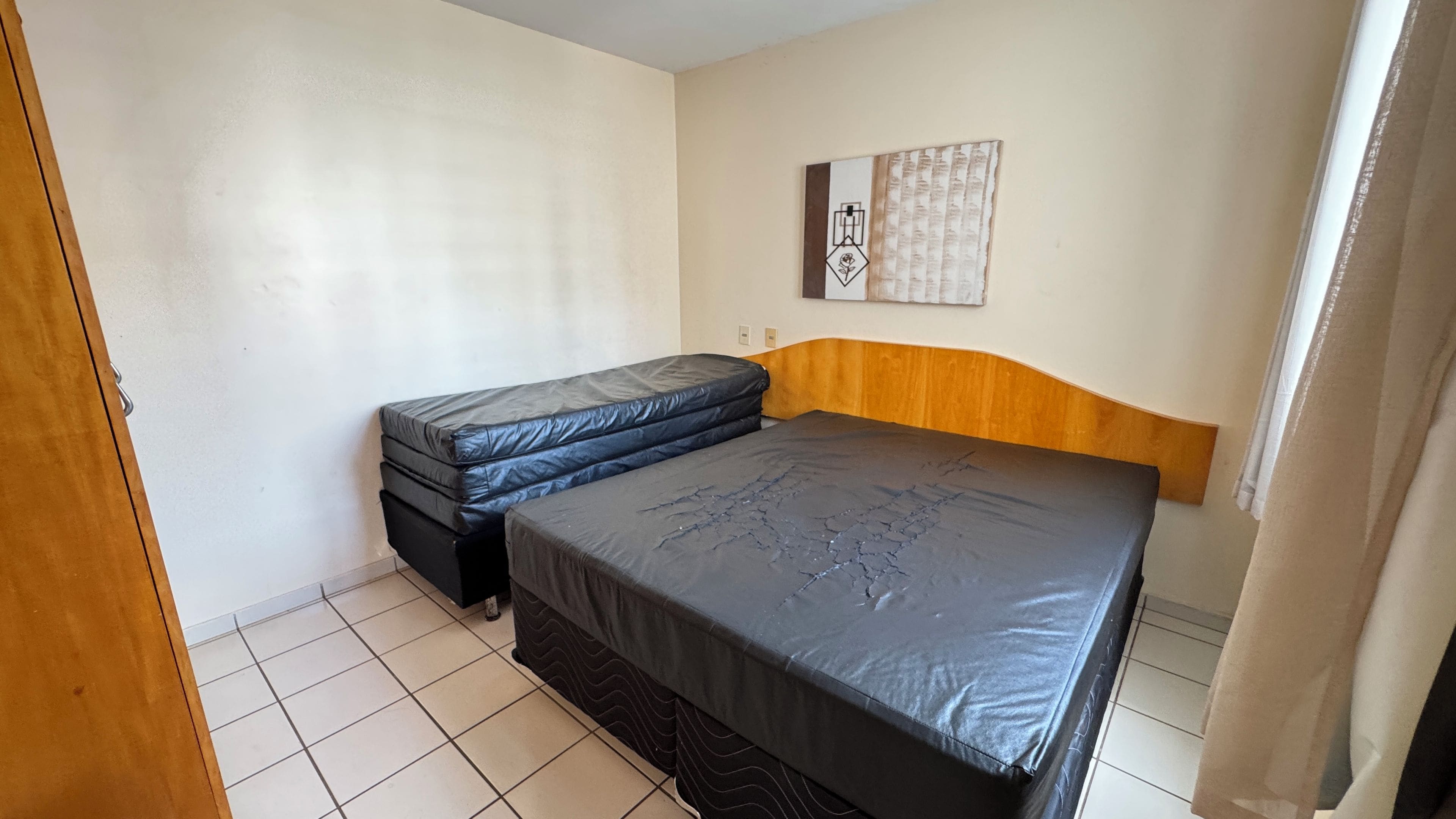 Una habitación pequeña con una cama individual, cabecera de madera, un colchón y una obra de arte en la pared.