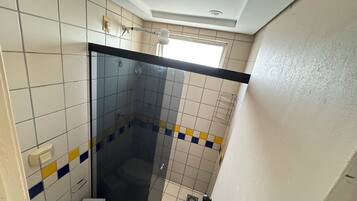 A small bathroom with a glass shower enclosure, tiled walls, and a window.