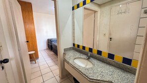 Un baño con encimera de granito, un lavabo, un espejo y una puerta que da a un dormitorio.