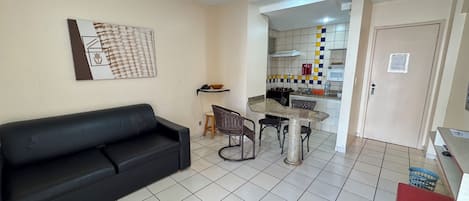 A living room with a black sofa, a dining table with four chairs, and a kitchen area with a microwave and a stove.