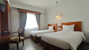 A hotel room with two beds, a desk, a chair, and a window with curtains.