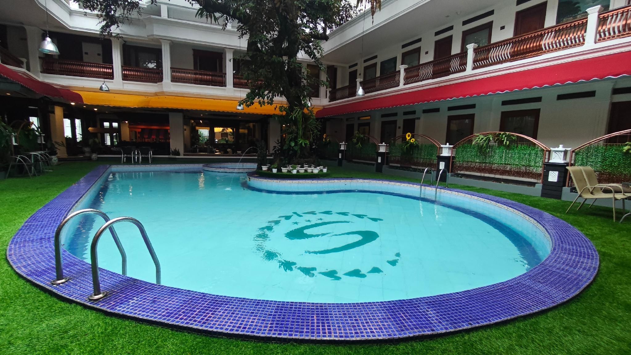 Una piscina interior con borde de azulejos, rodeada de césped artificial y un diseño decorativo en el centro.