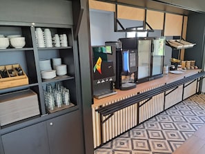 Une cuisine moderne équipée d’une machine à café, avec une pile d’assières et de verres.