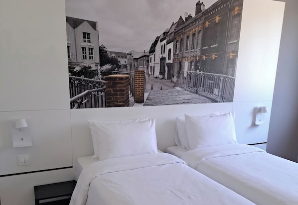 Una habitación de hotel con una cama, una lámpara de pared y un ventanal grande.