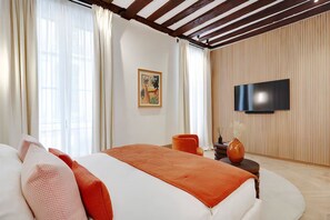 A hotel room with a bed, a TV mounted on the wall, and a window with curtains. - Elegant Saint-Germain Apartment with Refined Parisian Interiors (Paris)