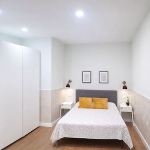 Une chambre à coucher comprenant un lit, deux tables de chevet, une armoire et deux lampes fixées au mur.