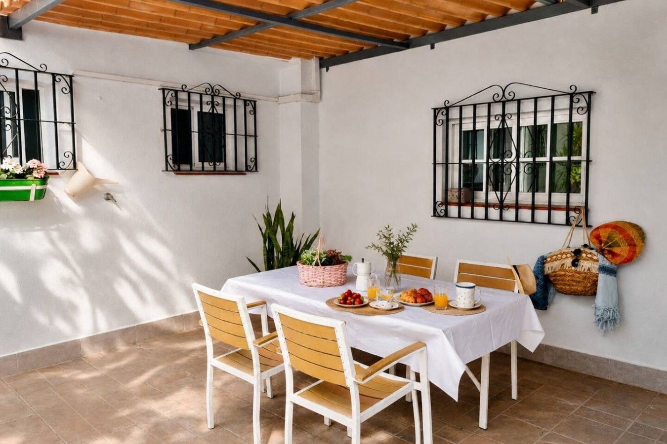 A dining area with a table set for breakfast, surrounded by chairs, with a white tablecloth, and a view of the outside through barred windows.