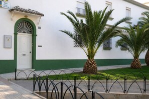 A building with a white facade, green trim, and a white door with a green arch. There are palm trees in front of the building. - 2 bedrooms | Large patio | 2-meter walk to the beach | Huelin (Málaga)