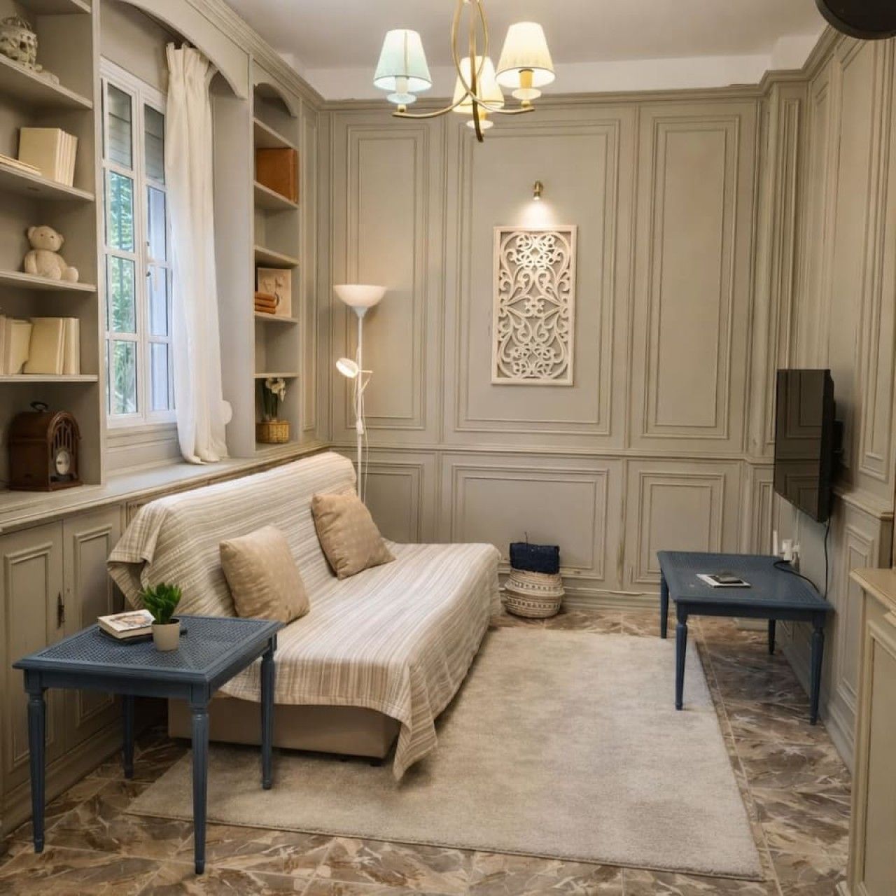 A room with a bed, two side tables, a window with curtains, a decorative wall piece, and a television mounted on the wall.