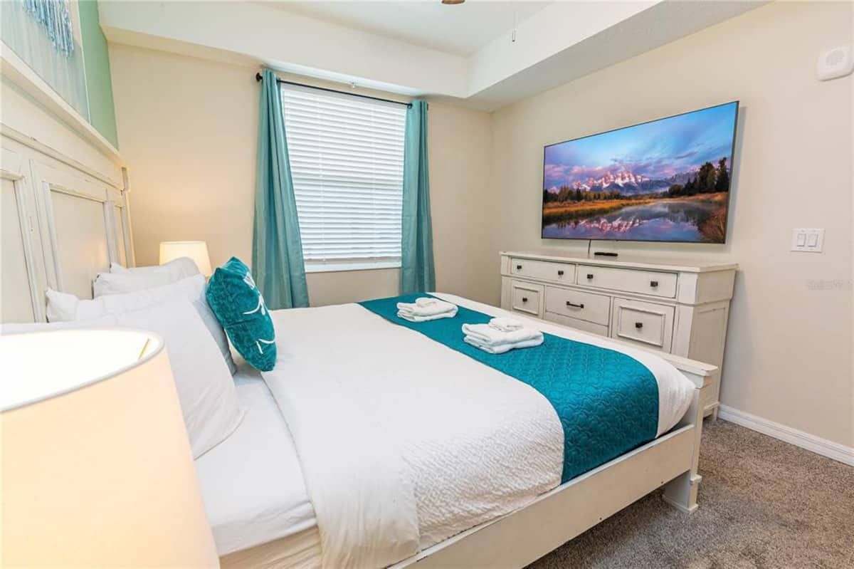 A hotel room with a bed, a television, a dresser, and a window with curtains.