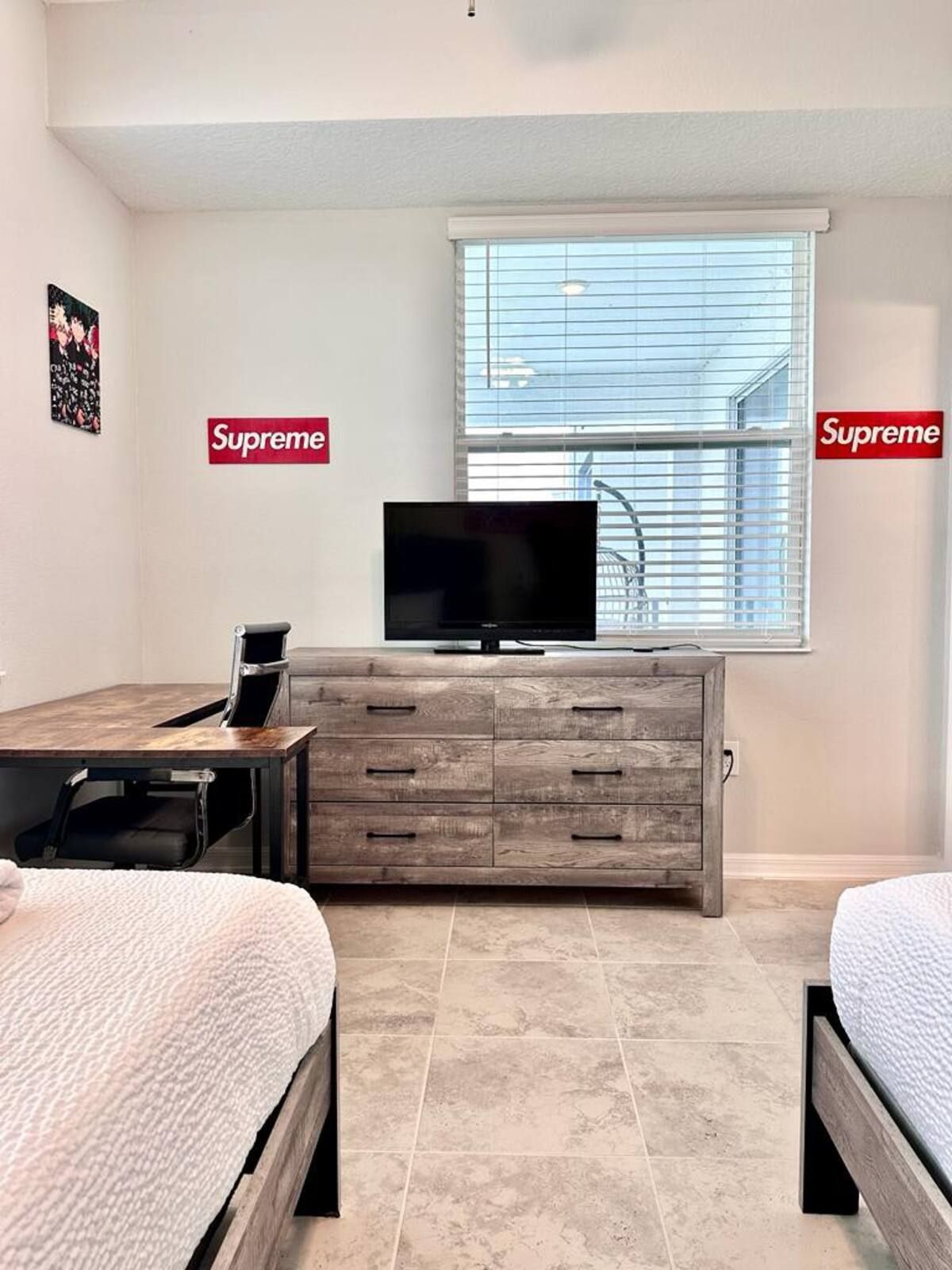 A bedroom with a bed, a TV on a wooden cabinet, and a window with blinds.