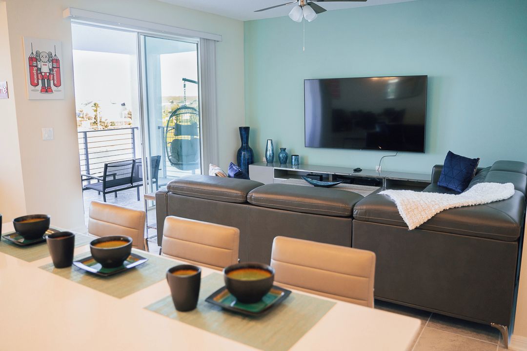 A modern living room with a flat-screen TV, a sofa, and a dining area with bowls of soup.