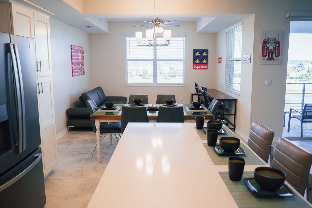 A modern kitchen with a dining area, a refrigerator, a ceiling fan, and a window with blinds.