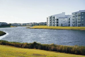 Un edificio moderno con varios pisos y balcones, ubicado junto a una masa de agua tranquila.