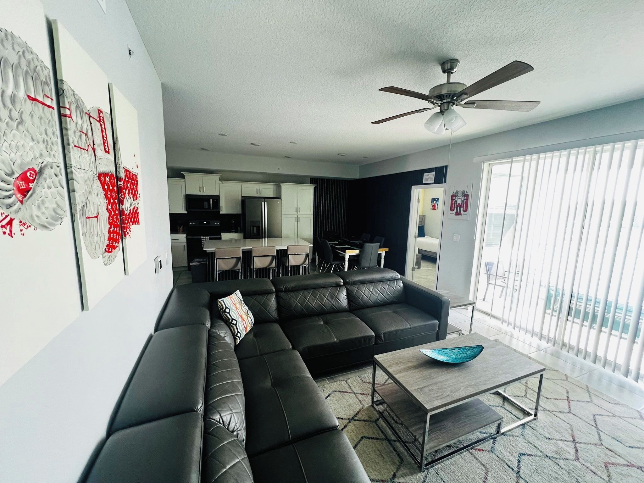 A modern living room with a black leather sofa, a coffee table, and a ceiling fan.