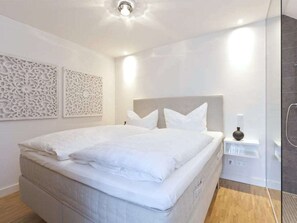 Ein modernes Schlafzimmer mit einem großen Bett, dekorativen Wandverkleidungen und einem Duschbereich.