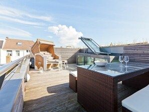 Eine Terrasse mit Tisch aus Glas, Korbmöbeln und einem überdachten Grillbereich.
