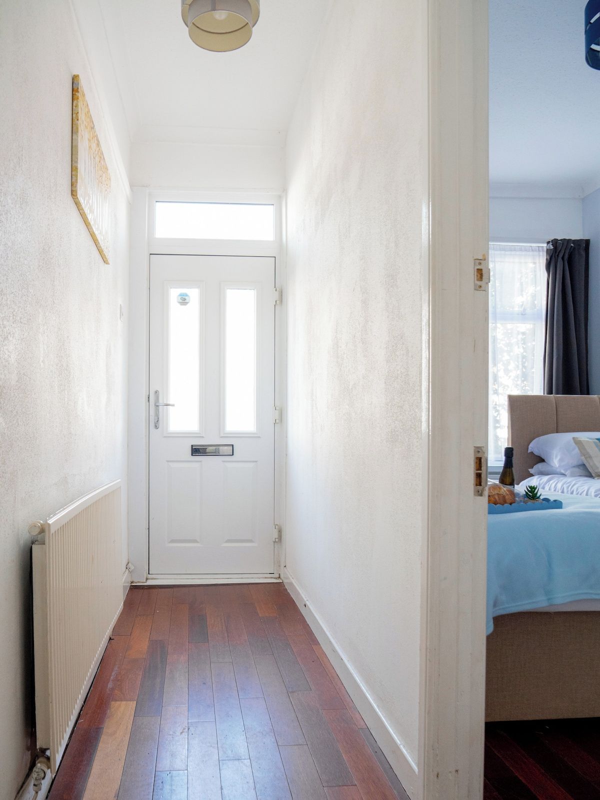 A hallway leading to a bedroom with a white door, a radiator, and a bed with a headboard.