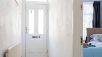 A hallway leading to a bedroom with a white door, a radiator, and a bed with a headboard.