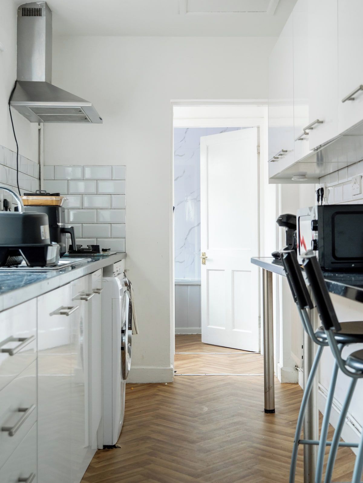 A modern kitchen with white cabinetry, a stainless steel range hood, a microwave, and a coffee machine.