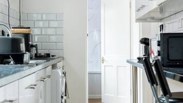 A modern kitchen with white cabinetry, a stainless steel range hood, a microwave, and a coffee machine.