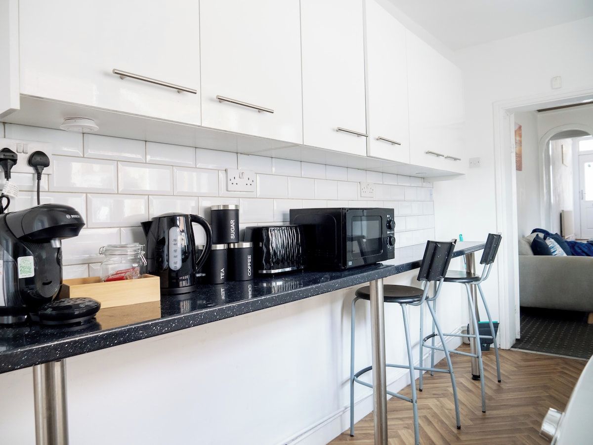 Cozinha moderna com armários brancos, bancada preta e um espaço para café.