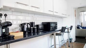 Cozinha moderna com armários brancos, bancada preta e um espaço para café.