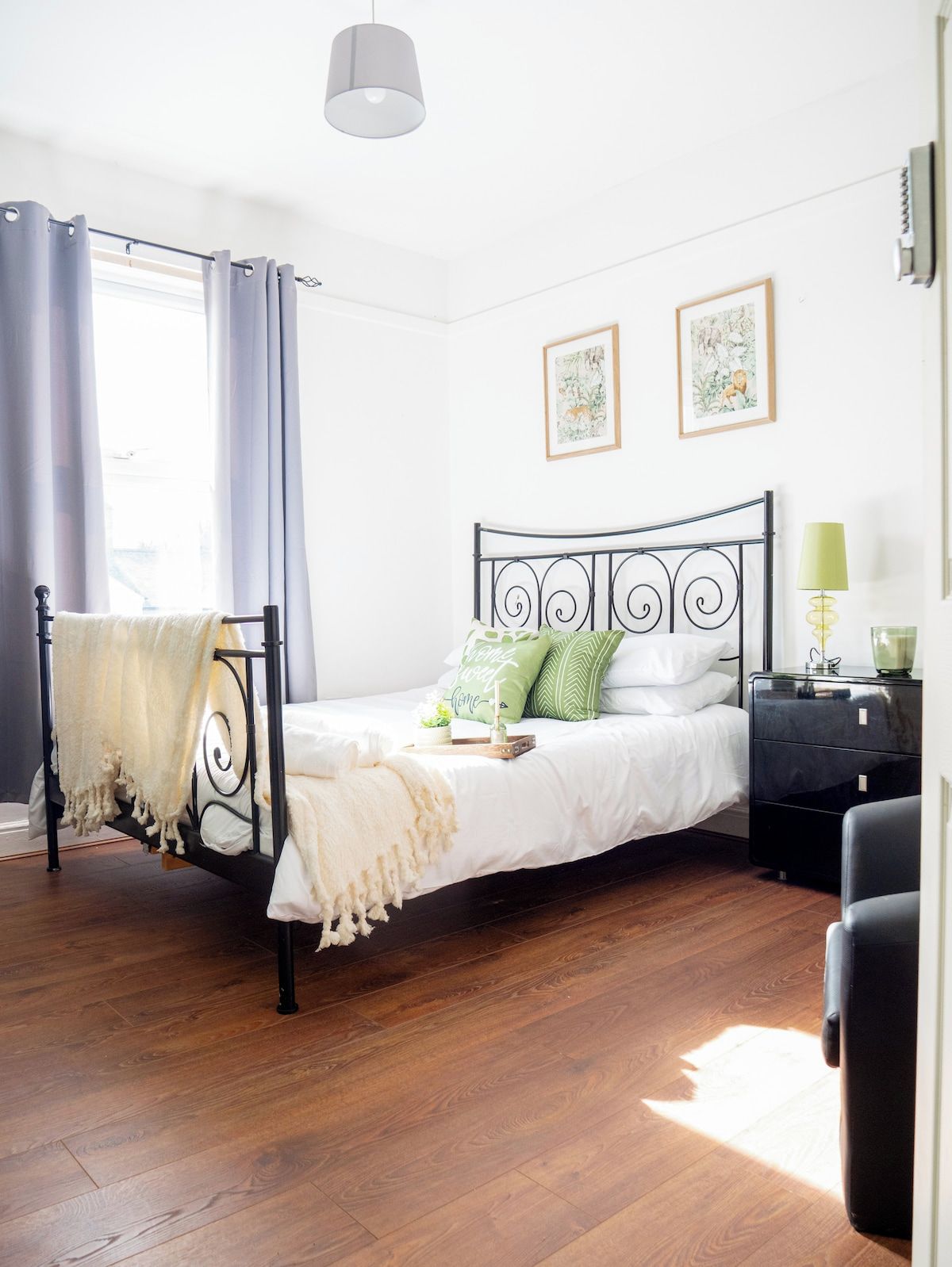 Quarto com uma cama, mesa de cabeceira, luminária e duas fotos emolduradas na parede.
