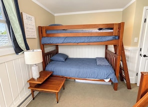 Ein Stockbett mit Holzrahmen und blauer Bettwäsche, ein Nachttisch mit Lampe sowie ein an der Wand befestigtes Schild mit Regeln für die Hütte.