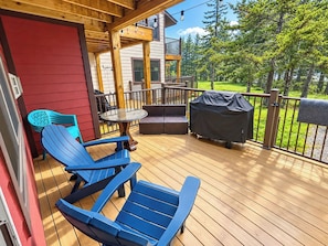 Eine Holzterrasse mit blauen Adirondack-Stühlen, einem Tisch und einem Grill.