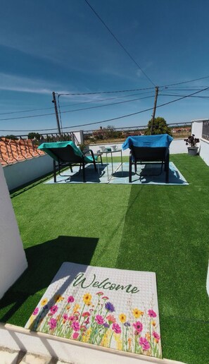 A rooftop terrace with artificial grass, two chairs, a table, and a welcome mat. - 2-bedroom house, office with sofa-bed, air con, wifi, garden shower, terrace (Cano)