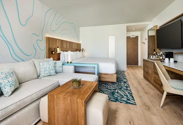 Ein modernes Hotelzimmer mit einer Couch, einem Holztisch, einem Bett mit Kopfteil, einem Schreibtisch mit Stuhl und einem großen Spiegel.