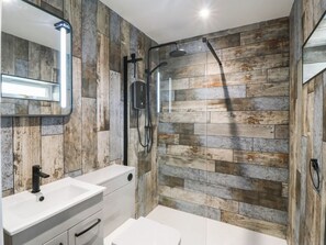 A bathroom with a wooden wall design, a white sink, and a shower area. - Angorfa (Pentraeth)