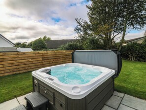 Ein Whirlpool in einem Garten mit Holzzaun, Rasen und einem Baum.