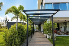 A covered walkway leading to a modern building with a glass facade. - Villa La Mar | Golf & Ocean Views, Private Pool (Punta Cana)