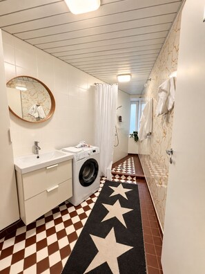 A compact hotel bathroom with a washing machine, a sink, a mirror, and a star-patterned rug. - 2-Bedroom apartment in the Hart of the city (Tallinn)