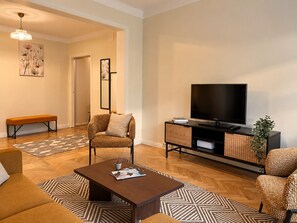 Ein modernes Wohnzimmer mit einer Couch, einem Couchtisch, einem Fernseher auf einem Schrank, einer Bank und einem gemusterten Teppich.