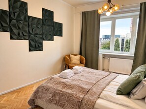 A hotel room with a bed, a chair, a window with curtains, and a geometric wall decoration. - 2-Bedroom apartment in the Hart of the city (Tallinn)