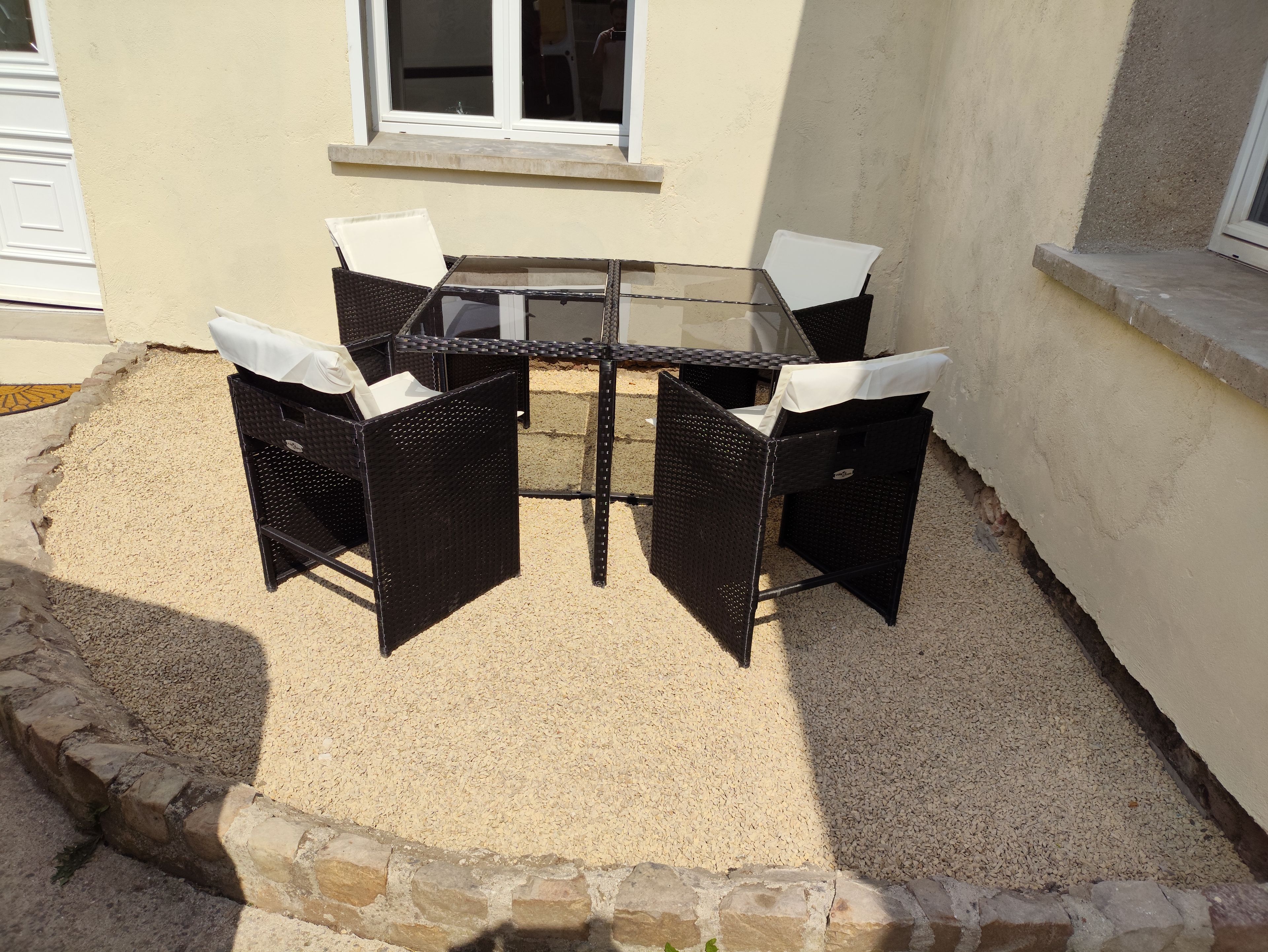Une terrasse dotée d’une table en verre et de quatre chaises, entourée d’une zone recouverte de gravier et bordée de pierres.