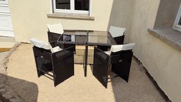 Une terrasse dotée d’une table en verre et de quatre chaises, entourée d’une zone recouverte de gravier et bordée de pierres.