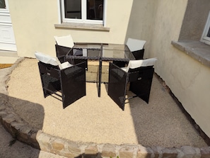 A patio with a glass table and four chairs, surrounded by a gravel area and a stone border.
