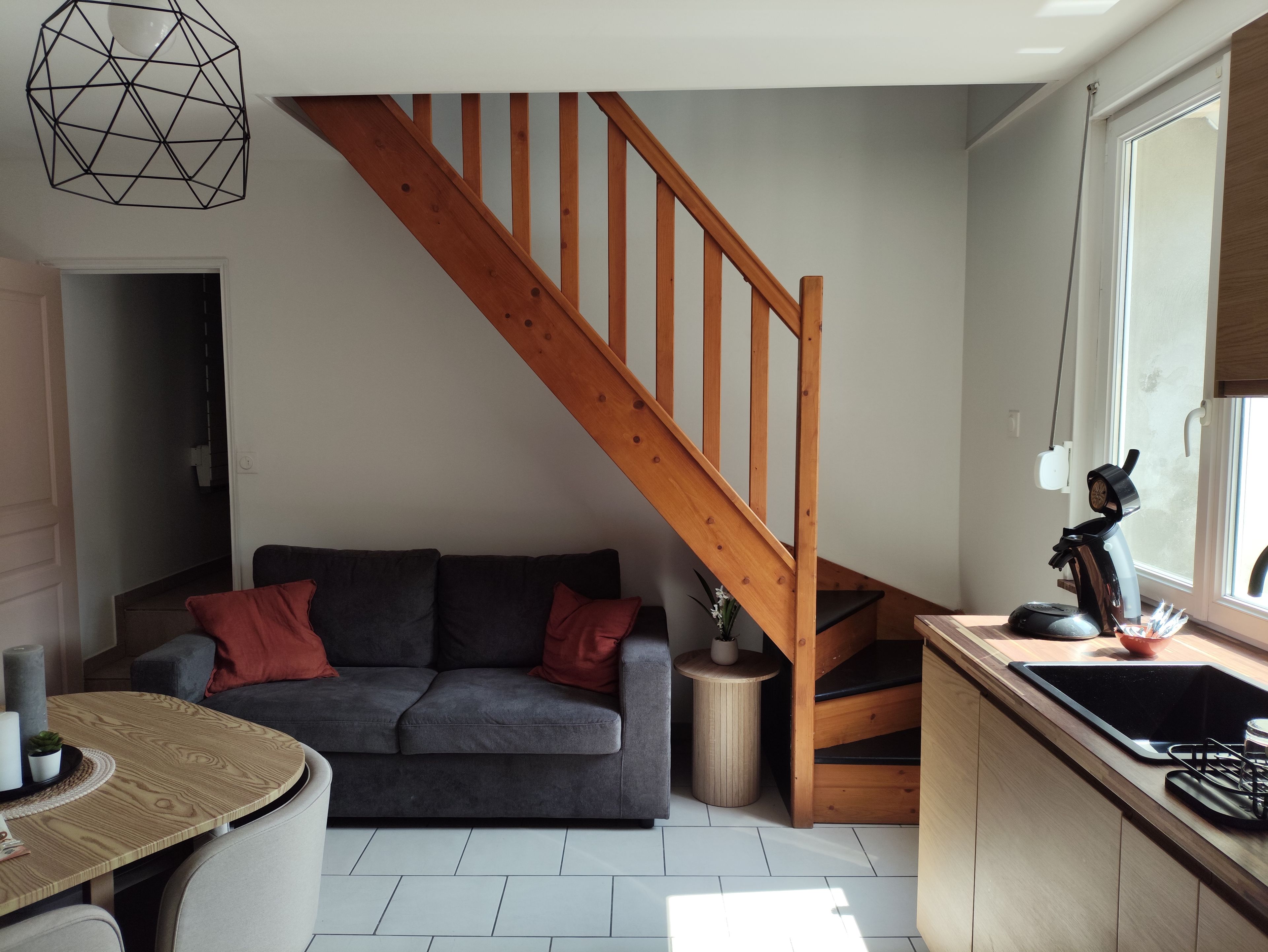 Un espace de vie moderne avec un escalier en bois, un canapé gris et un coin cuisine équipé d’un évier et d’une cuisinière.