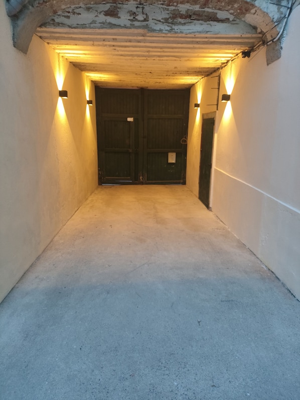 Un pasillo estrecho y poco iluminado con suelo de hormigón y dos puertas cerradas al final.